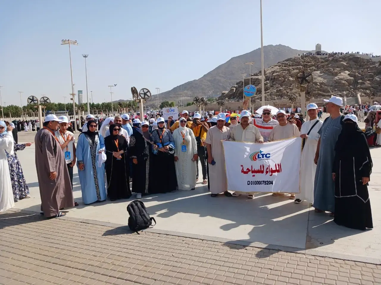 مجموعة من عملاء اللواء للسياحة يرفعون لافتة الشركة عند جبل الرحمة بعرفات